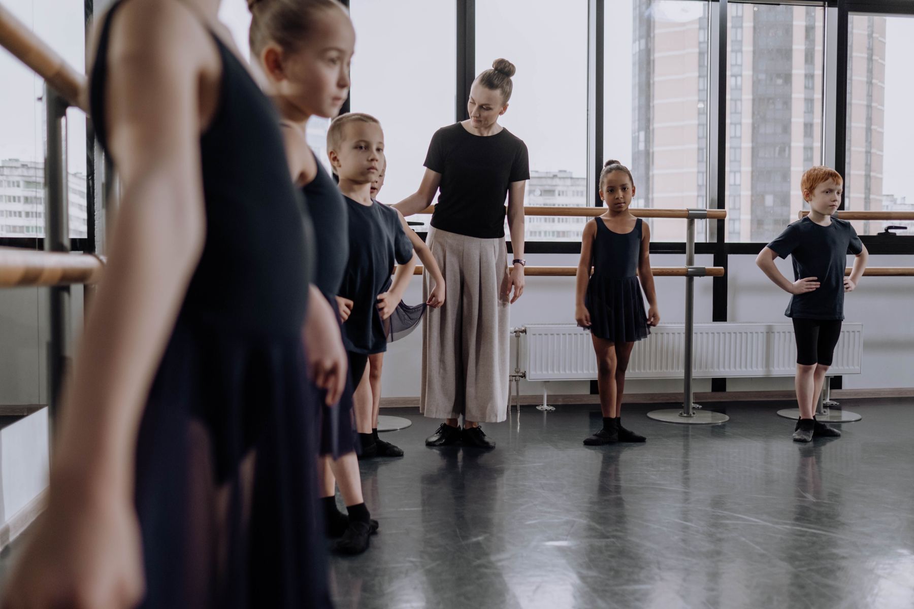 A teacher guiding a class of young dancers standing in first position in a bright studio