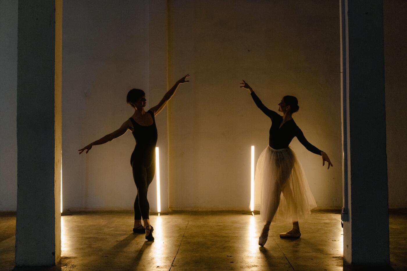 Two ballet dancers reaching toward each other between warm strip lights