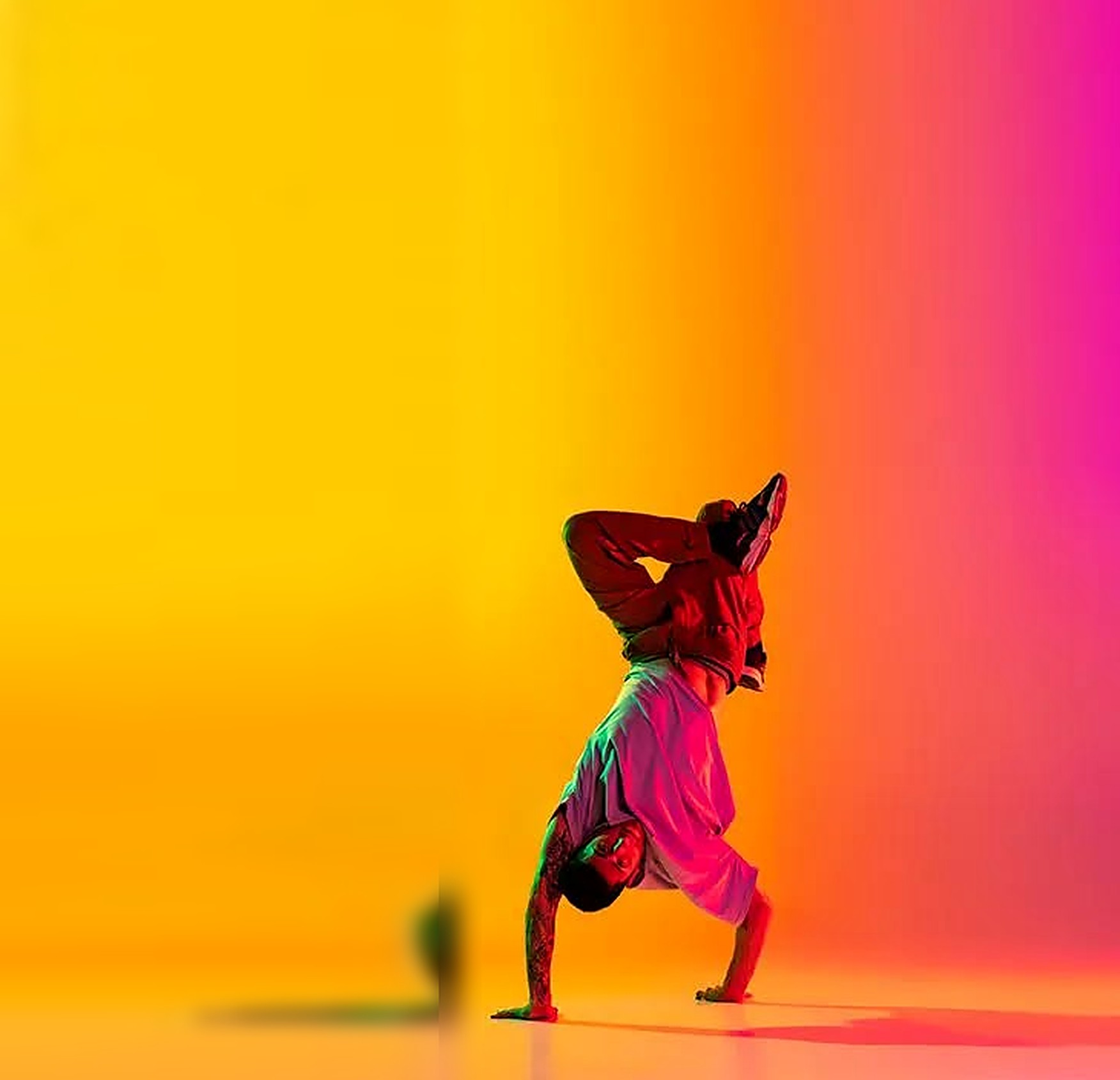 A breakdancer balancing on one hand against a vivid yellow and magenta wash