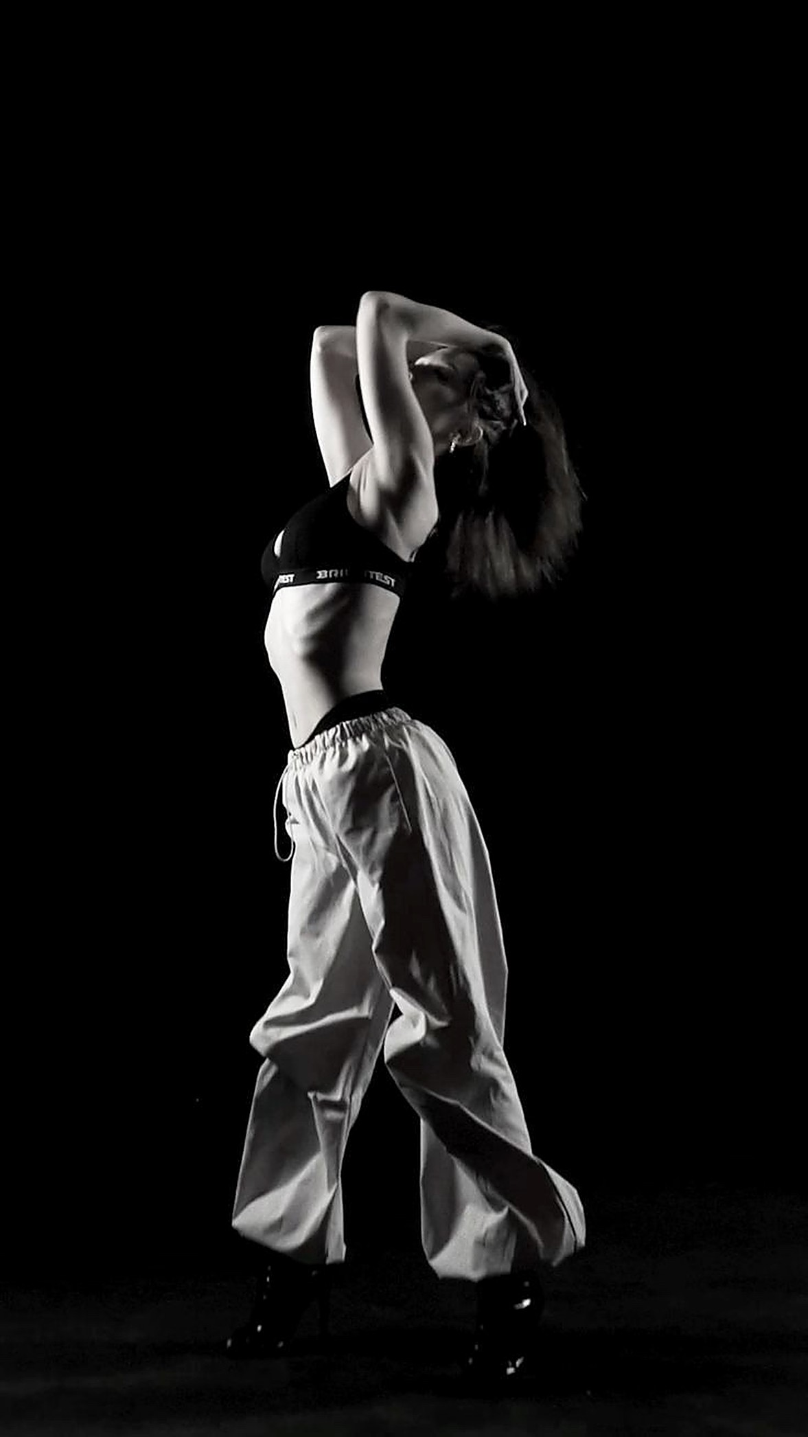 A dancer mid-move against a black stage, photographed in black and white