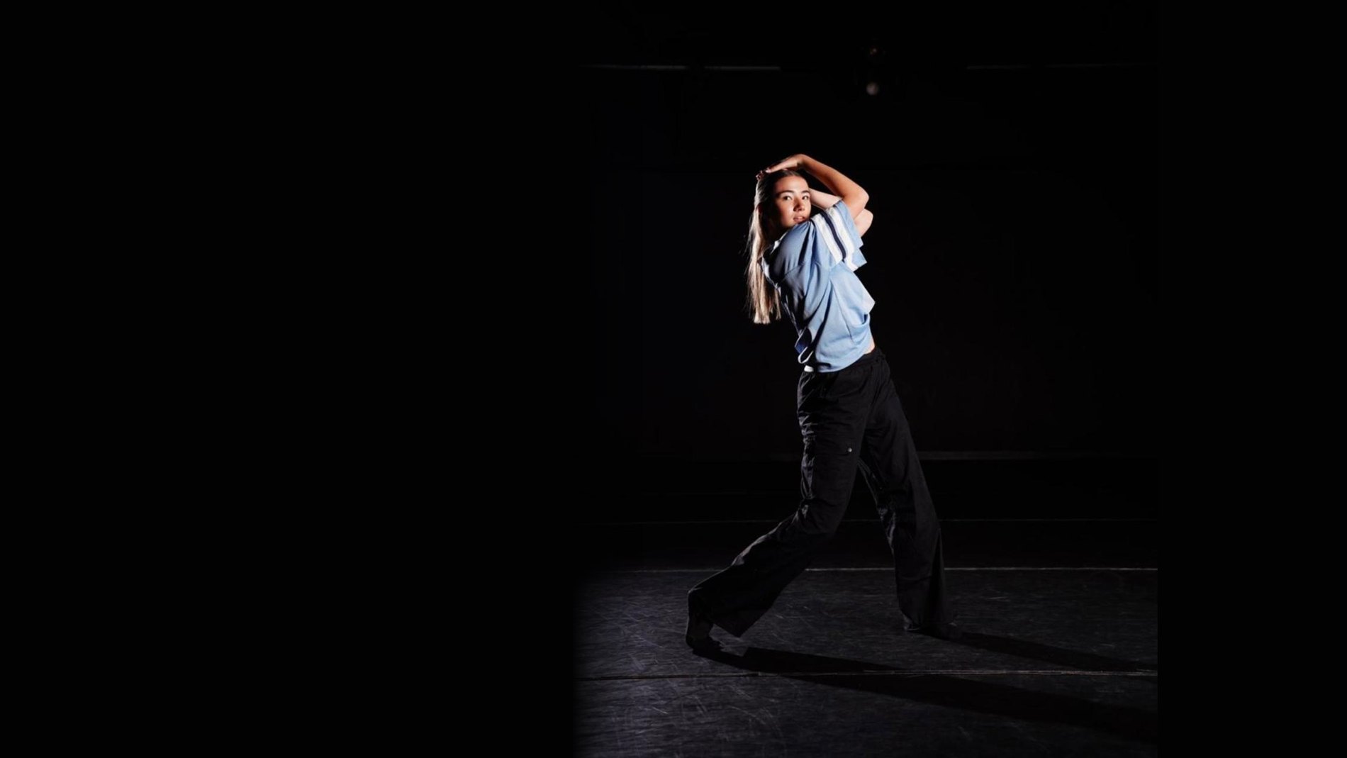 A dancer mid-phrase on a dark stage, caught in a single shaft of light