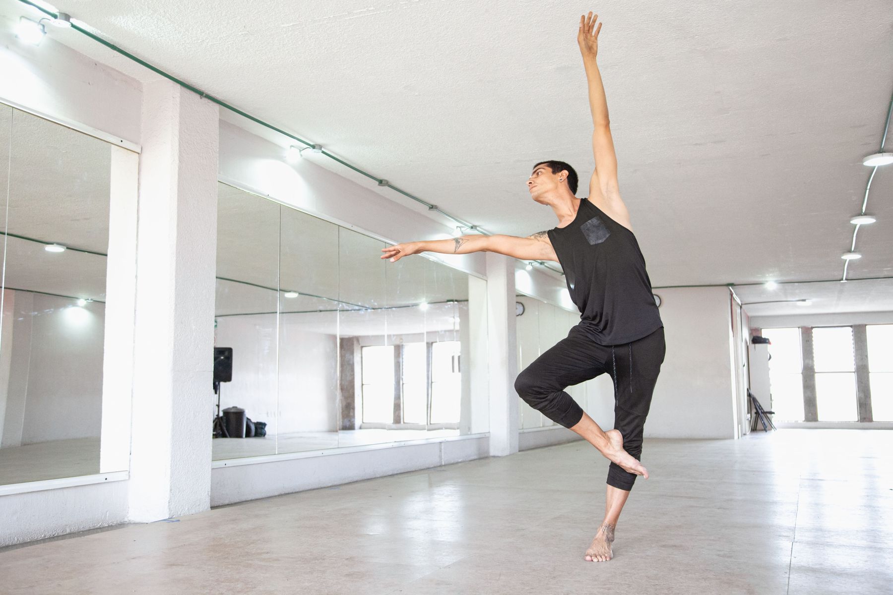 A dancer rehearsing alone in a bright mirrored studio, arms extended