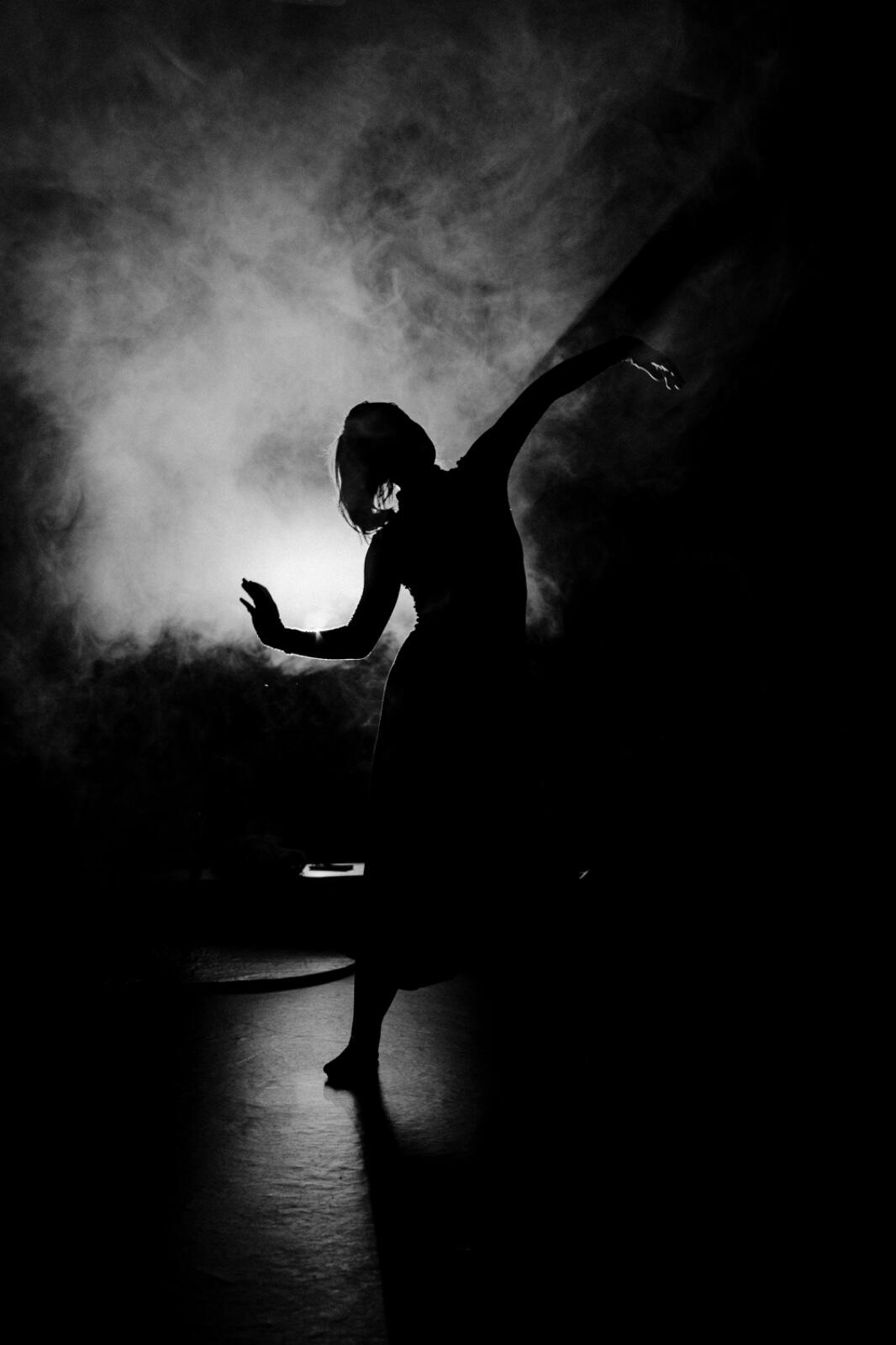 A dancer silhouetted mid-turn in a beam of stage light and smoke