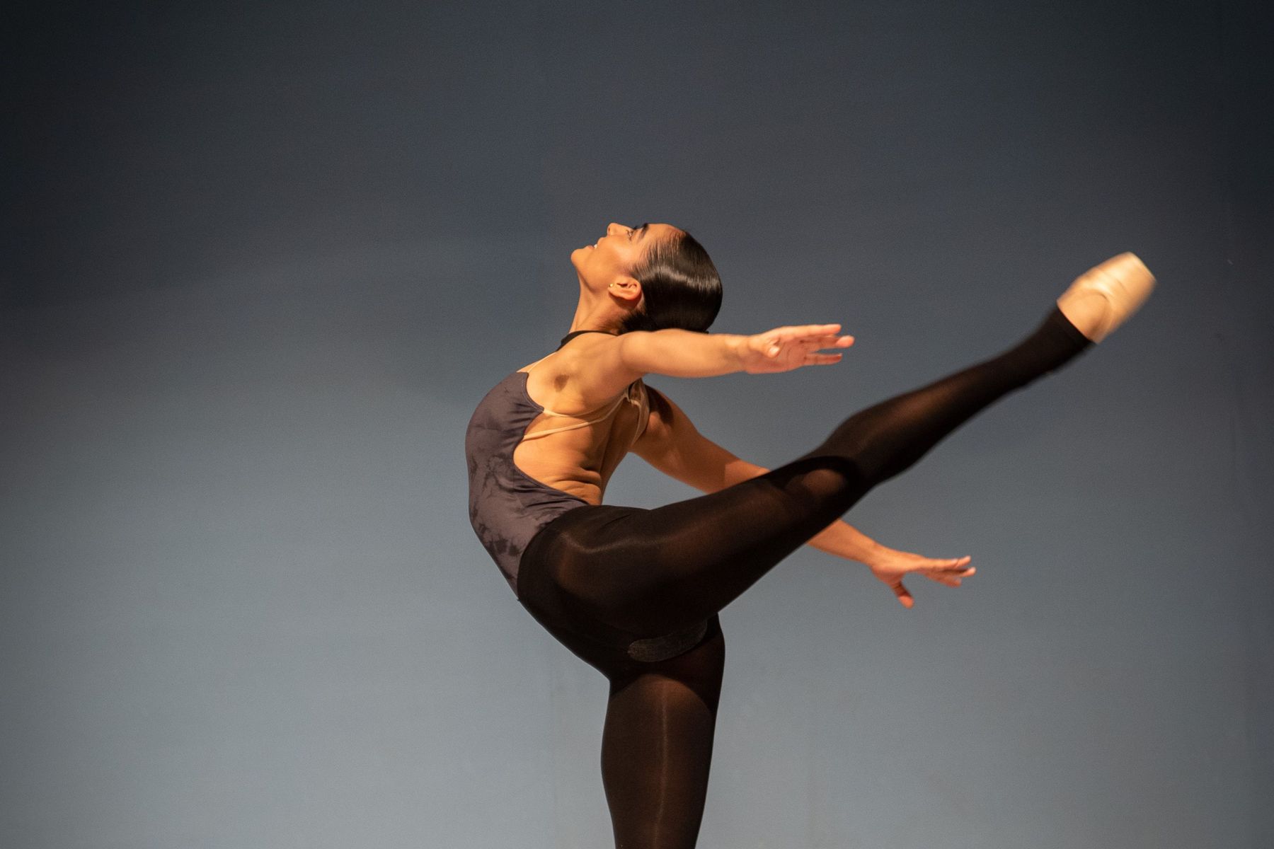 A ballerina on stage in a deep arabesque, one leg extended high, en pointe